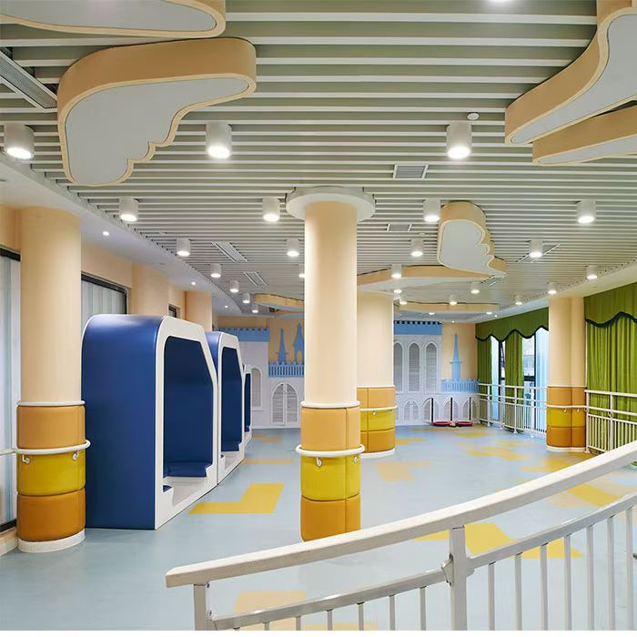 Light-colored linear ceiling baffles with curved decorative features and pale yellow columns in a children’s activity interior
