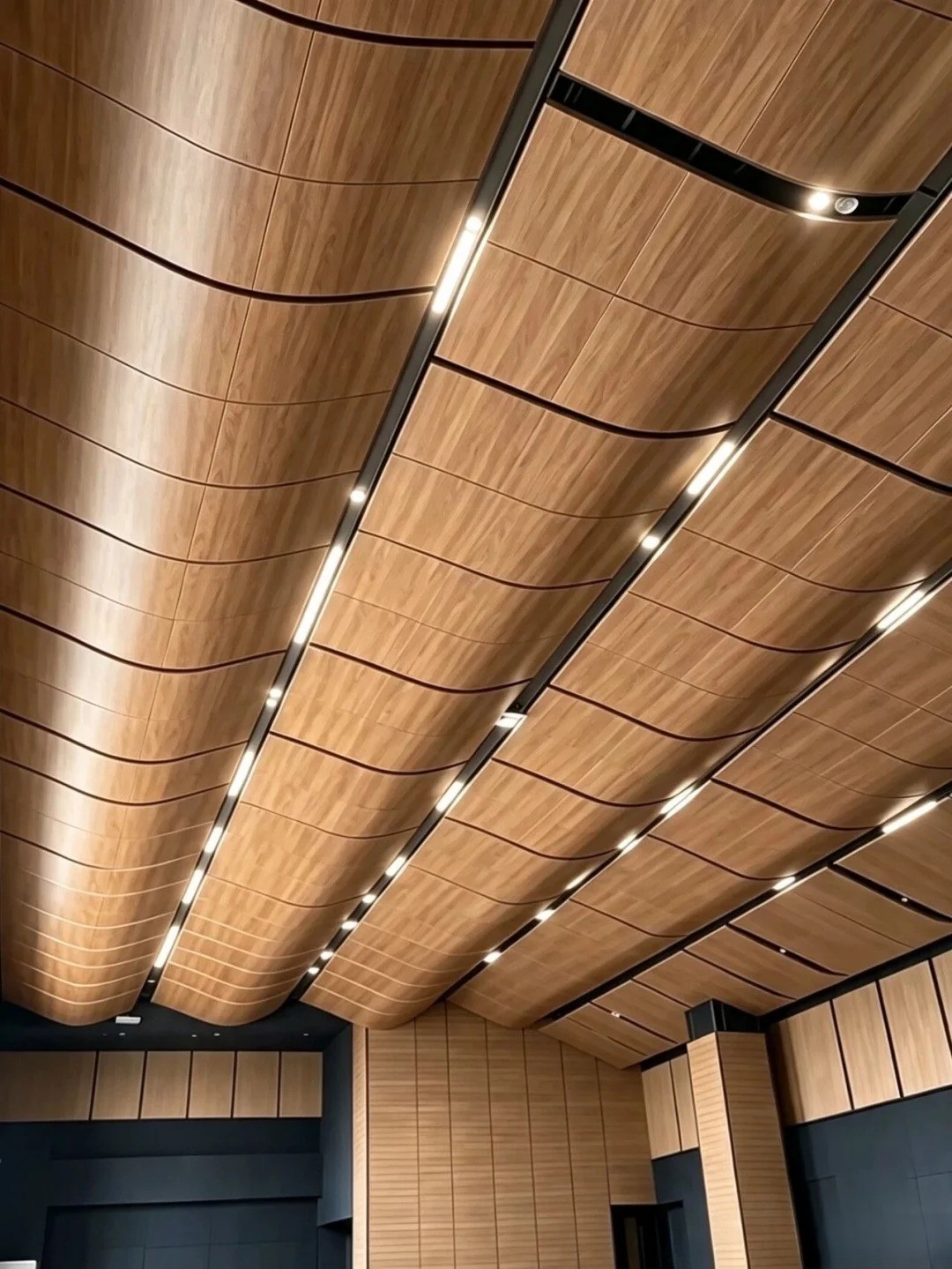 Wood-grain single-curved aluminum ceiling panels arranged in parallel waves with recessed lighting